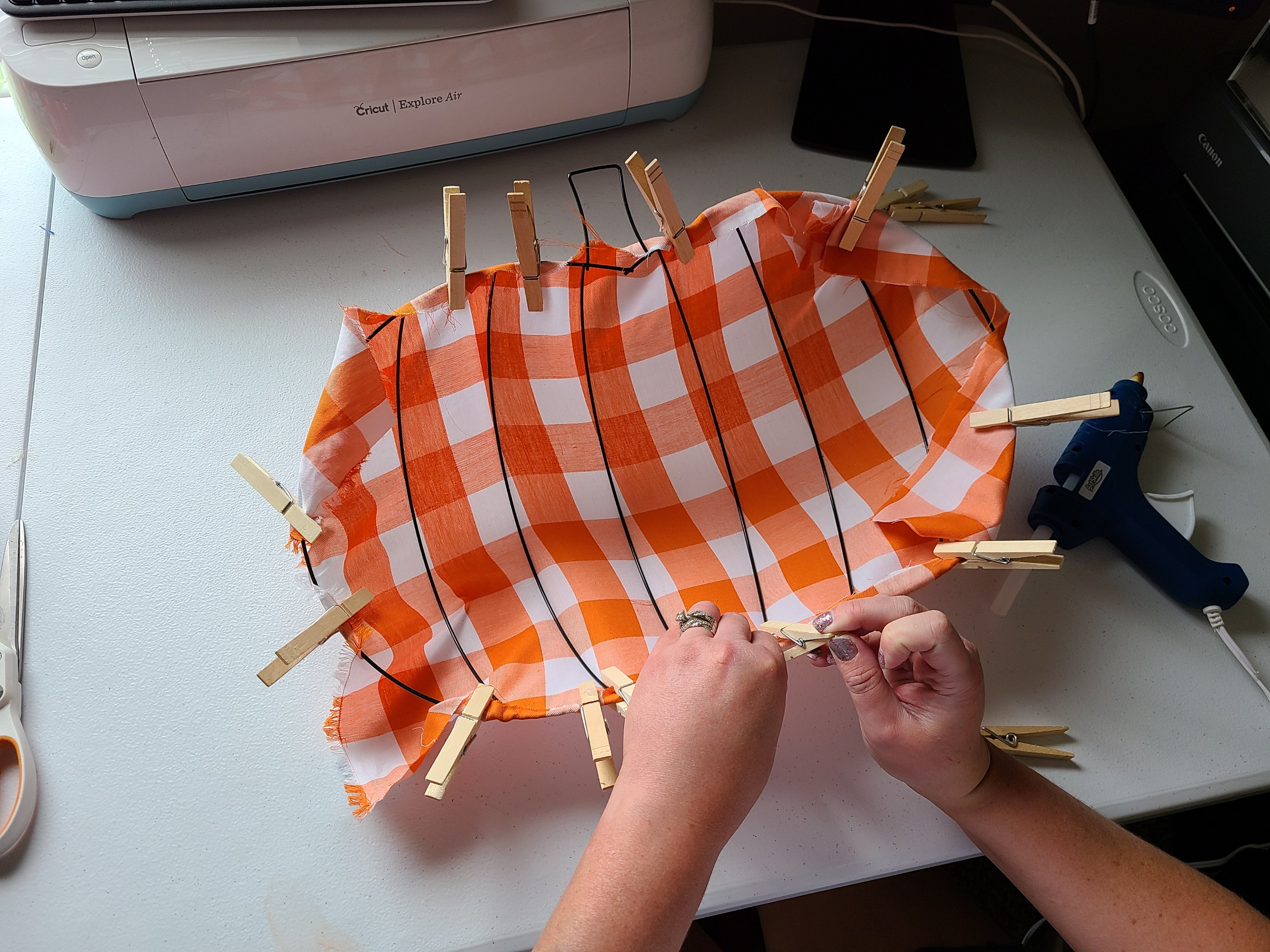 Placing a clothespin the fabric to the bottom wire on the Dollar Tree pumpkin wreath form after hot glue was added.