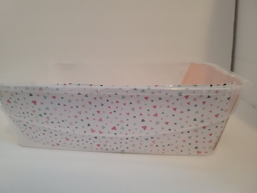 Clear bin lined with heart patterned cardstock paper with a list of items that will be placed inside printed on a pink cardstock paper in the front of the bin facing out.