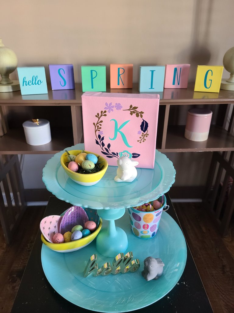 DIY two tier tray with Easter and spring decor on it with canvas blocks in the background that say "hello" and spell out "spring."