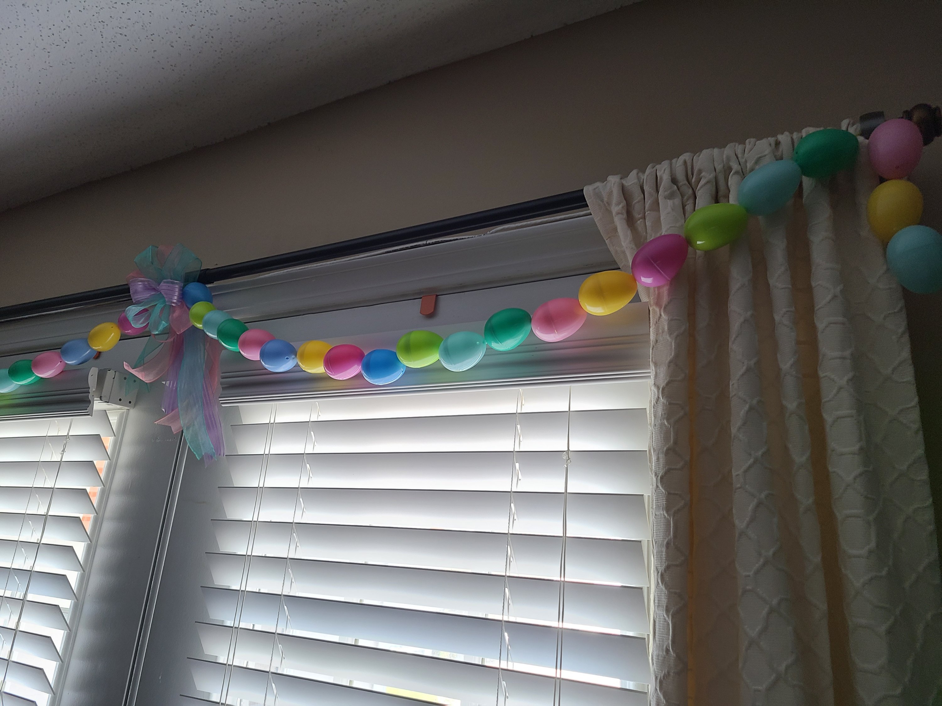 Easter egg garland with a lavender, pink, and aqua bow in the center and colored eggs extending out of each side, with the phot focusing on the right side where the garland drops down the side of ivory curtains.