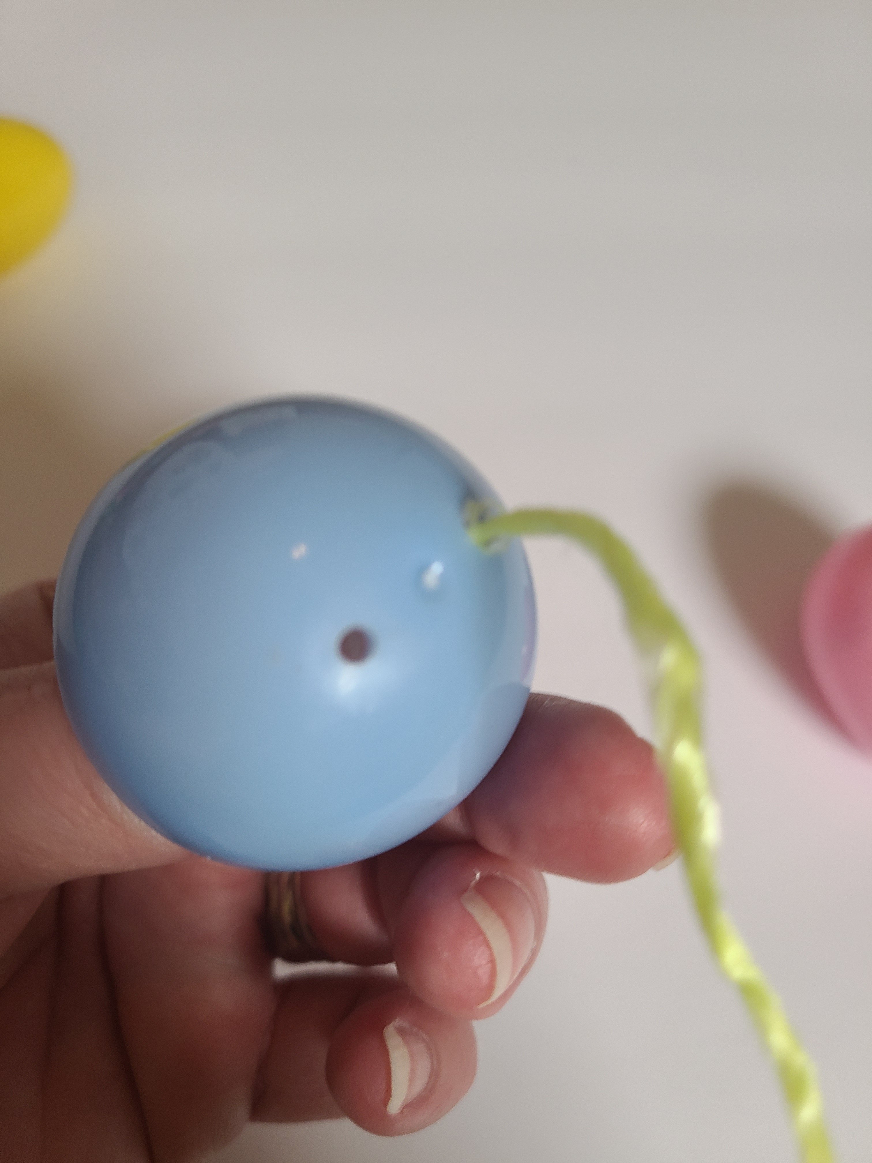 Showing the bottom of a plastic Easter egg where there are two holes to string the twine through to make the garland.
