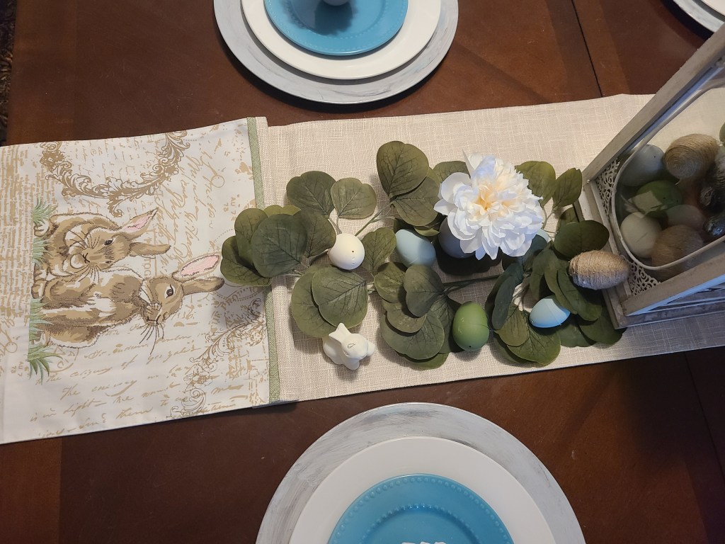 Easter tablescape with rabbit table runner with greenery, chalk painted eggs, and egg vases with white flower.
