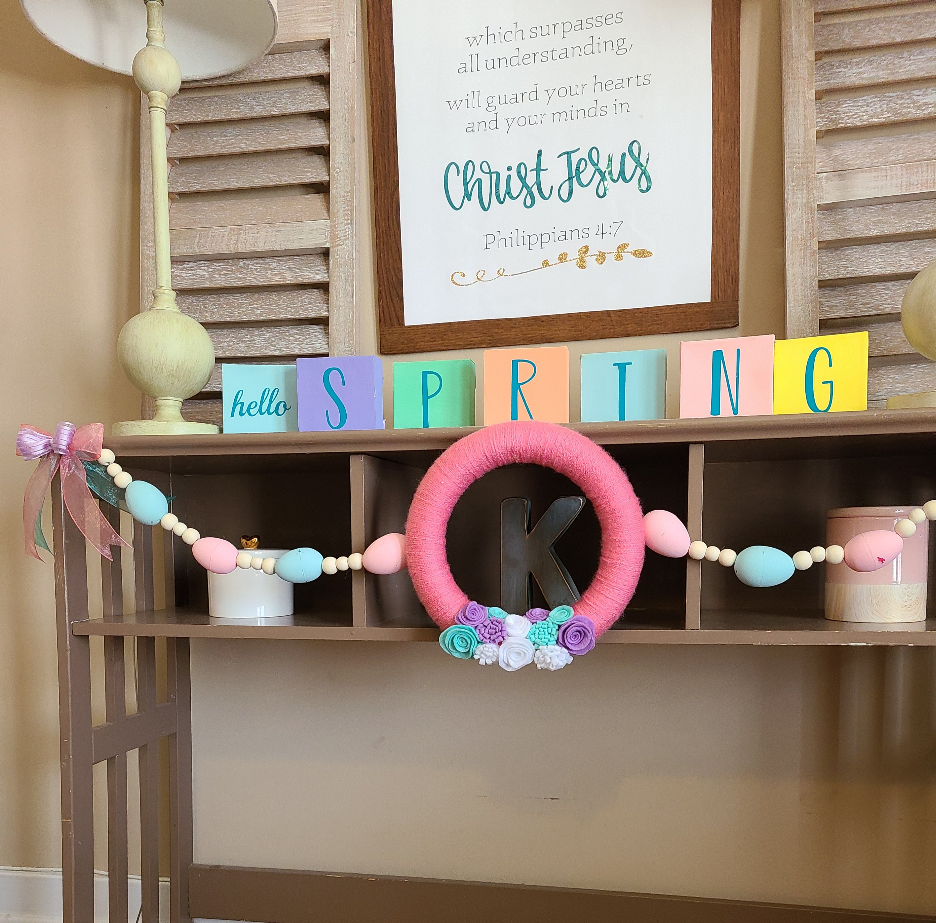 A spring garland with a pink yarn wreath in the center with baker's twine extending from both sides with pink and blue Easter eggs and wood beads strung between them.