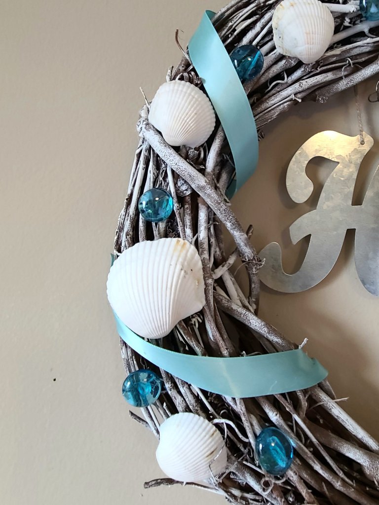 Close up picture of the side of the beach wreath. Grapevine form with white seashells, blue gems, and satin ribbon.
