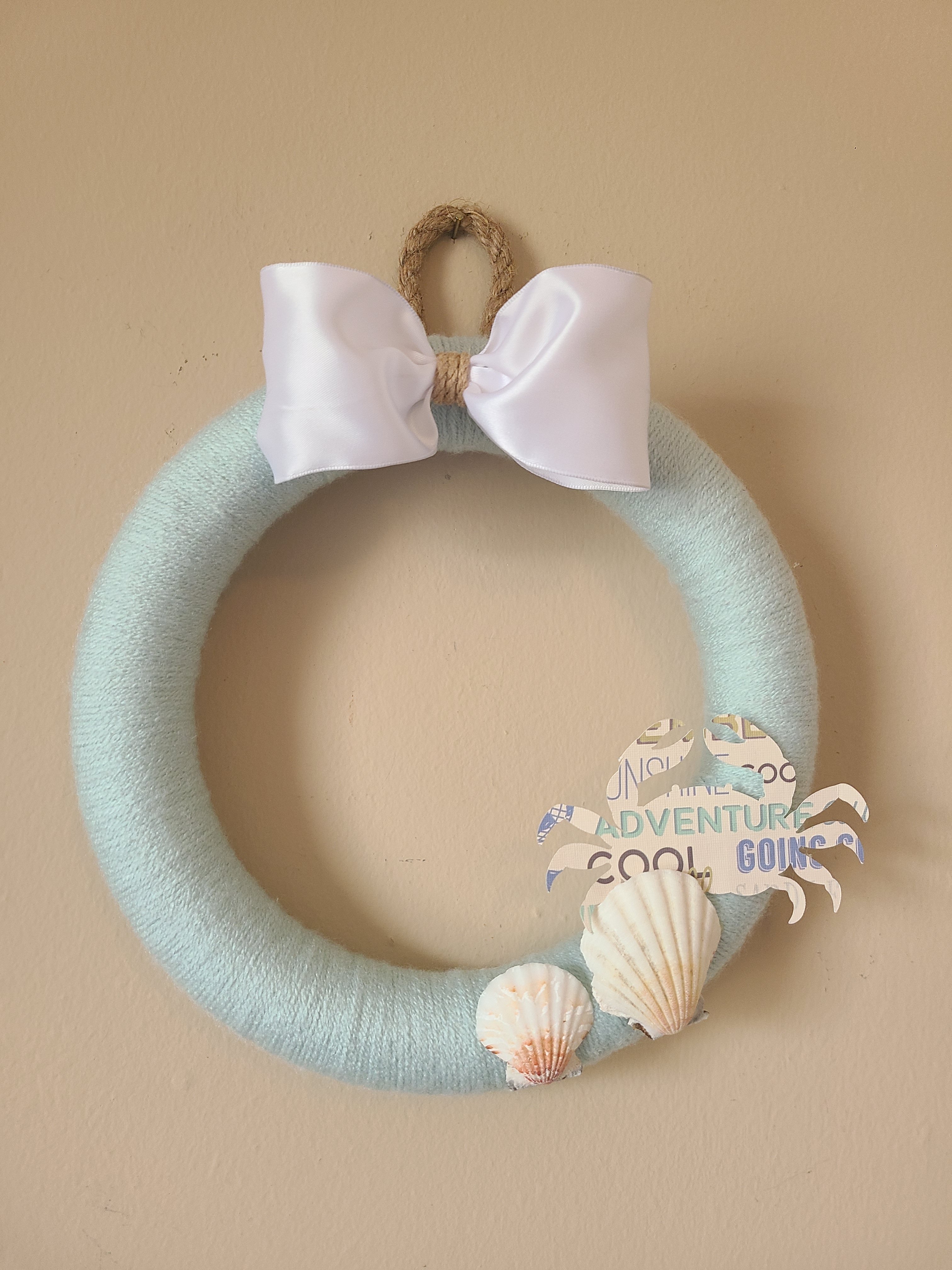 DIY Yarn wreath made with light robin's egg blue yarn, seashells, a white bow, and nautical rope.