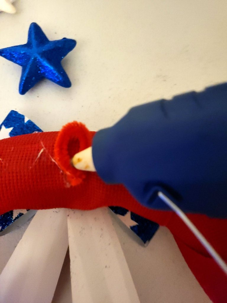 Red pipe cleaner twisted to form a loop and being hot glued to the back of the DIY patriotic wreath.
