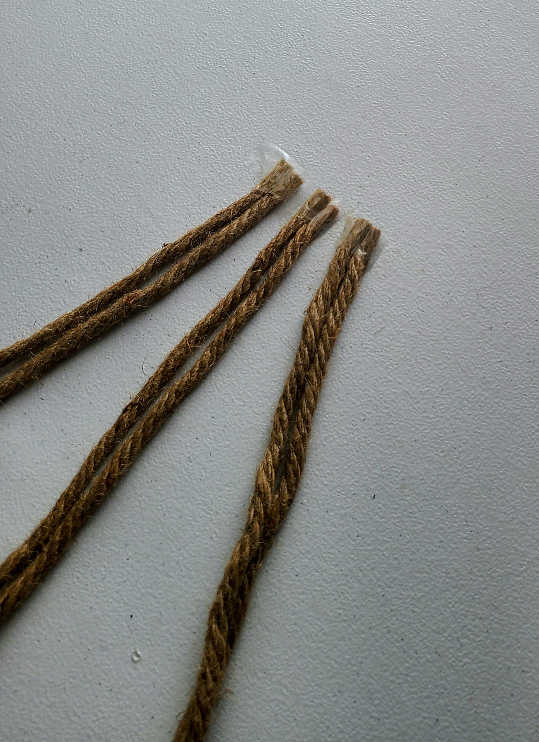 Two sisal ropes laid up against each other with the ends taped to the table next to two other sets of two to make it easier to braid together for the nautical rope wreath.
