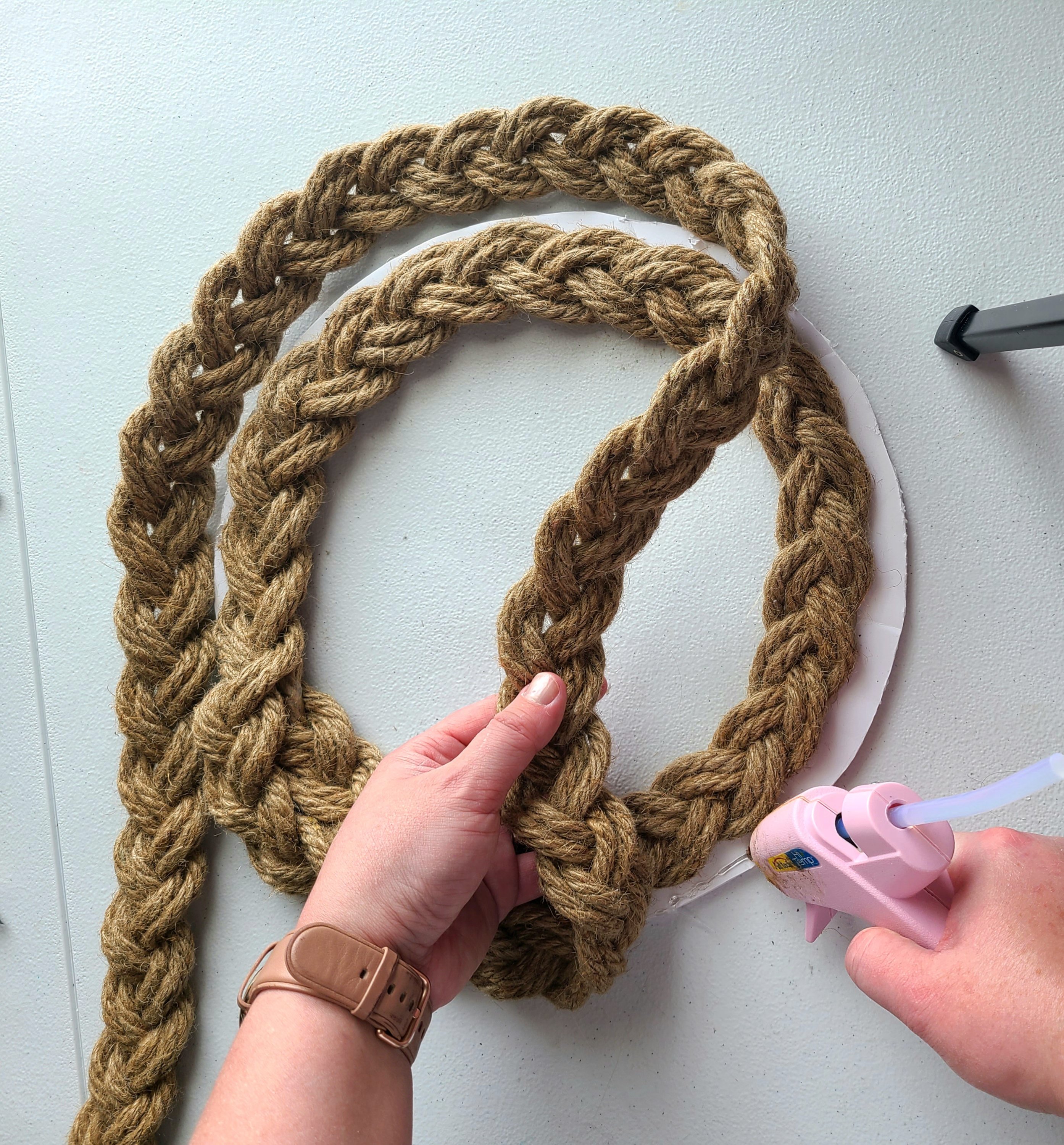 Putting hot glue on the outside of the wreath form to place the braided rope on as a 2nd row.