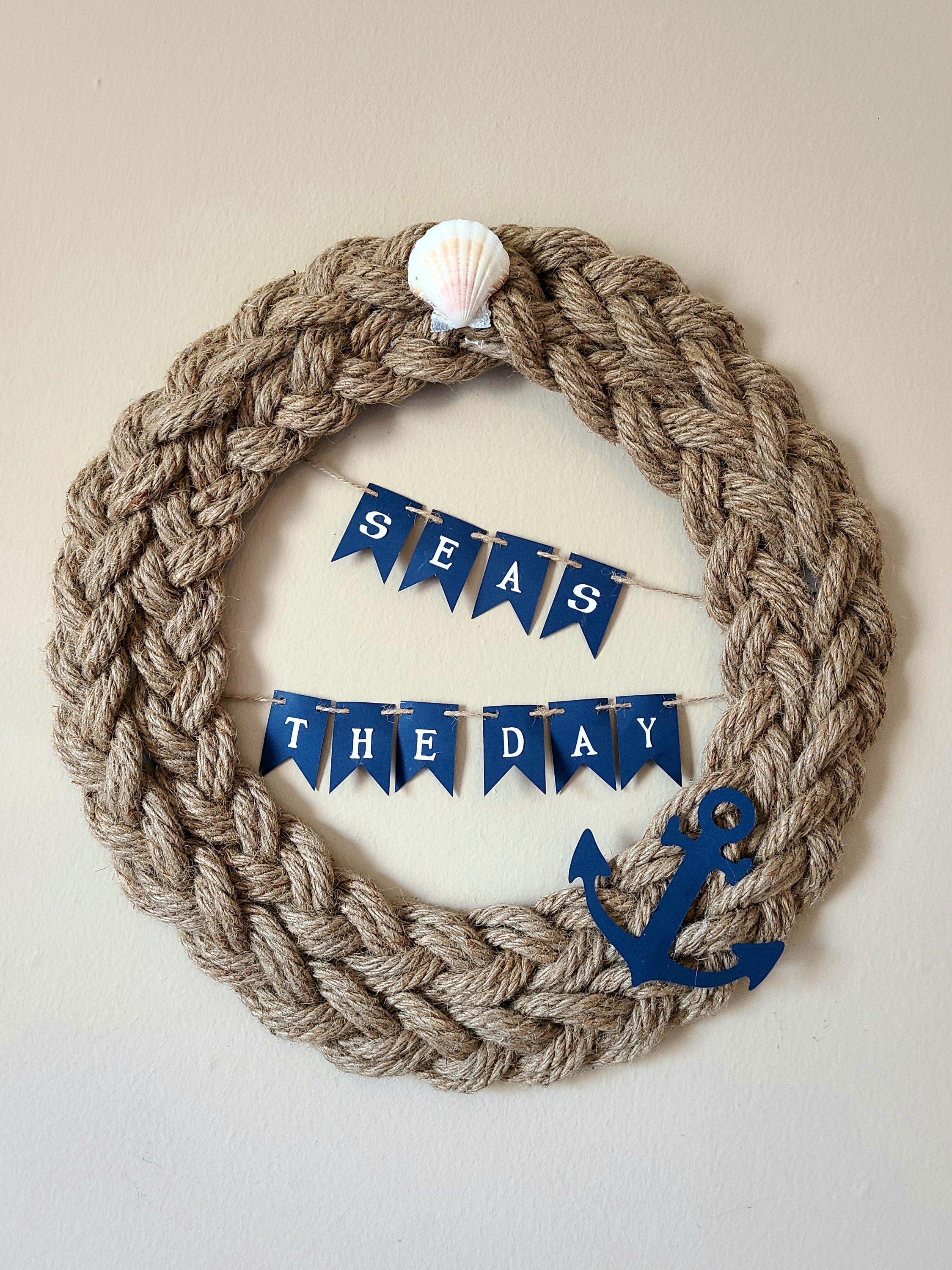 Completed nautical rope wreath: braided sisal rope glued to a DIY wreath form with a white seashell added to the top and a banner that reads, "seas the day," strung across the center, and a navy blue anchor shape glued to the wreath at about 5 o'clock.