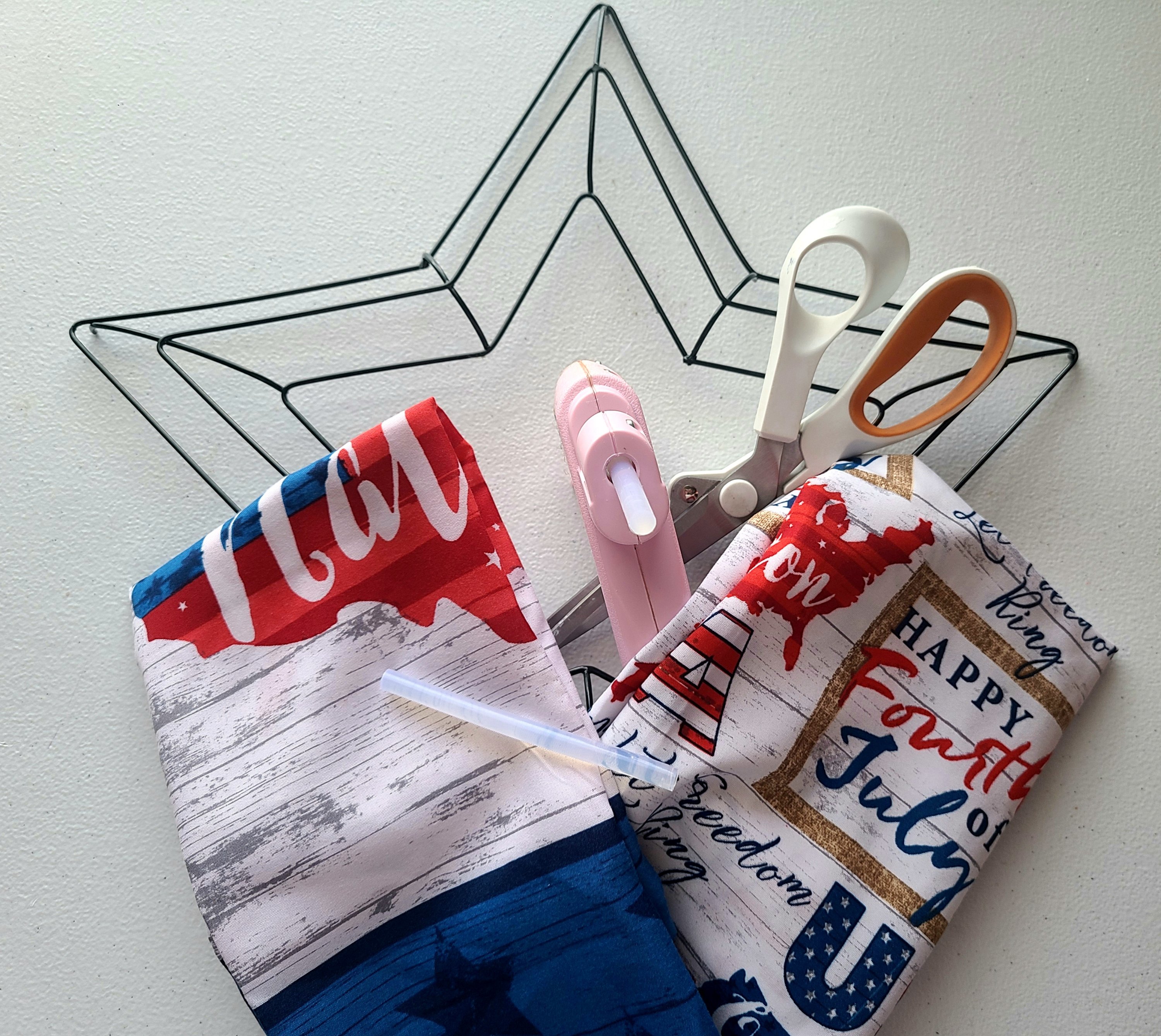 Patriotic star wreath supplies: star wreath form, scissors, hot glue gun & glue, and two bandanas made of patriotic fabric from Dollar Tree