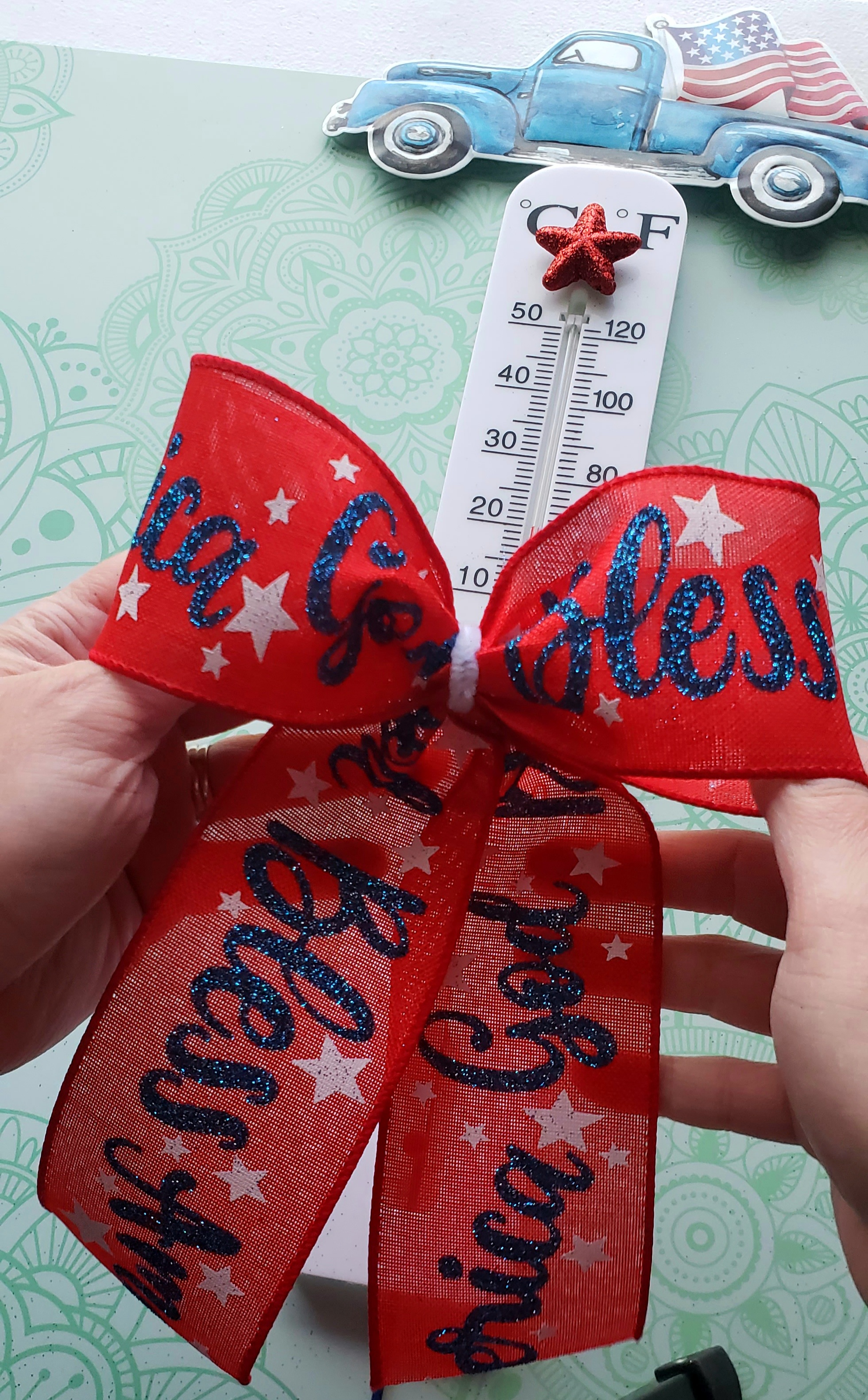 A bow made with patriotic ribbon to place at the bottom of the red, white, and blue outdoor thermometer.