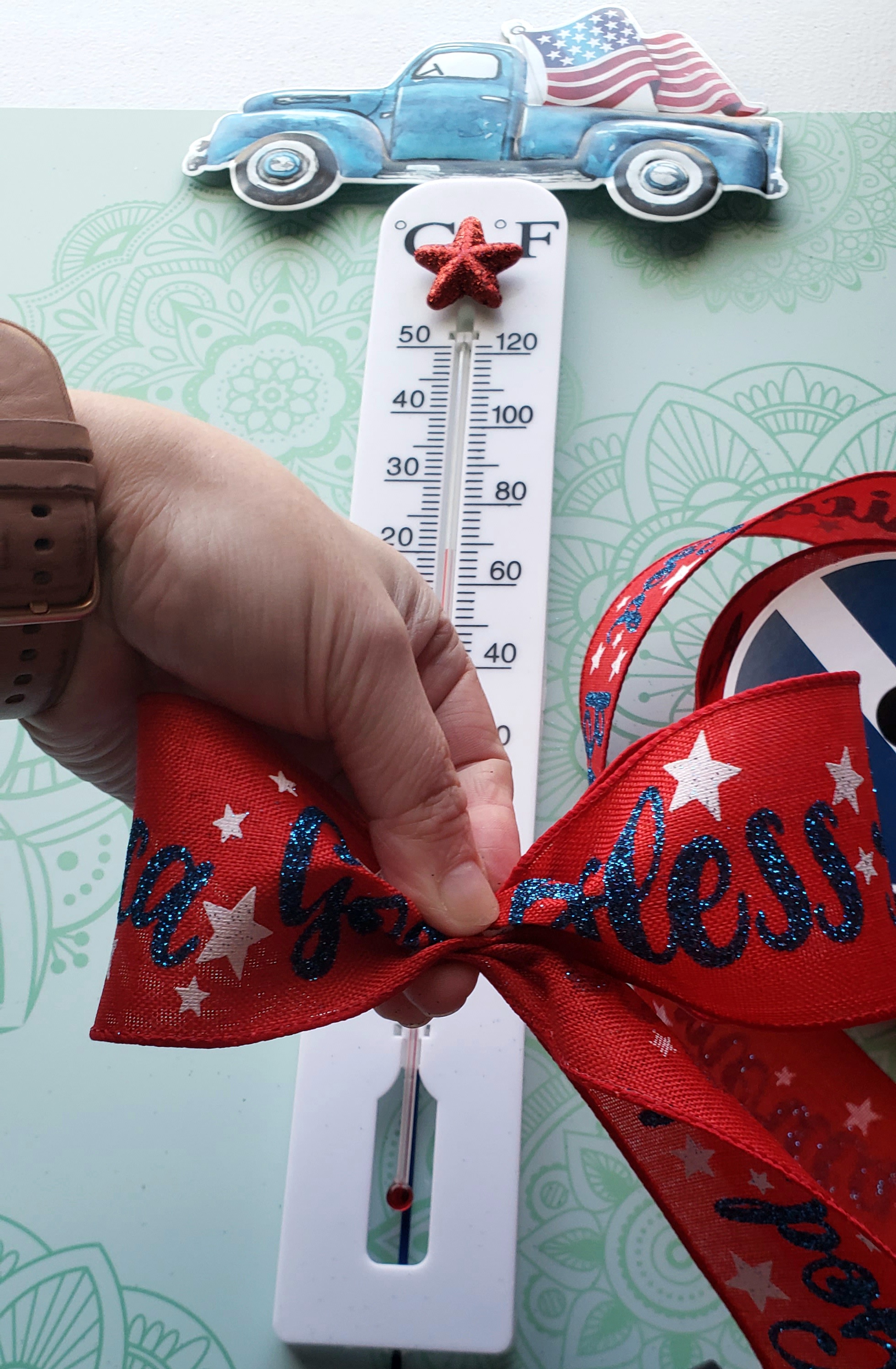 Forming two loops with red, white, and blue ribbon to make a bow for the bottom of the patriotic outdoor thermometer DIY.