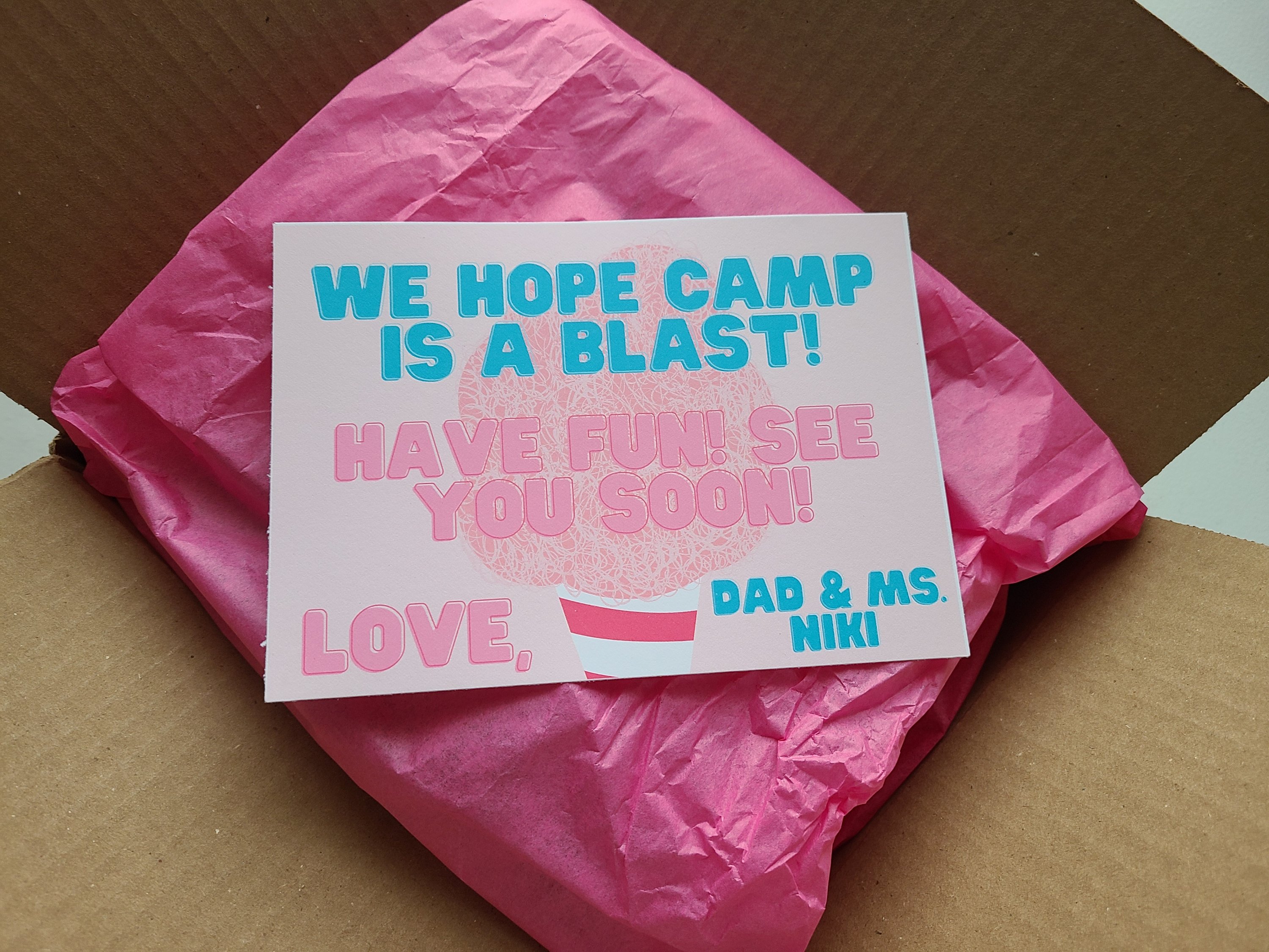 A girl's summer camp care package in a box with a free printable on top addressing the package to a girl.