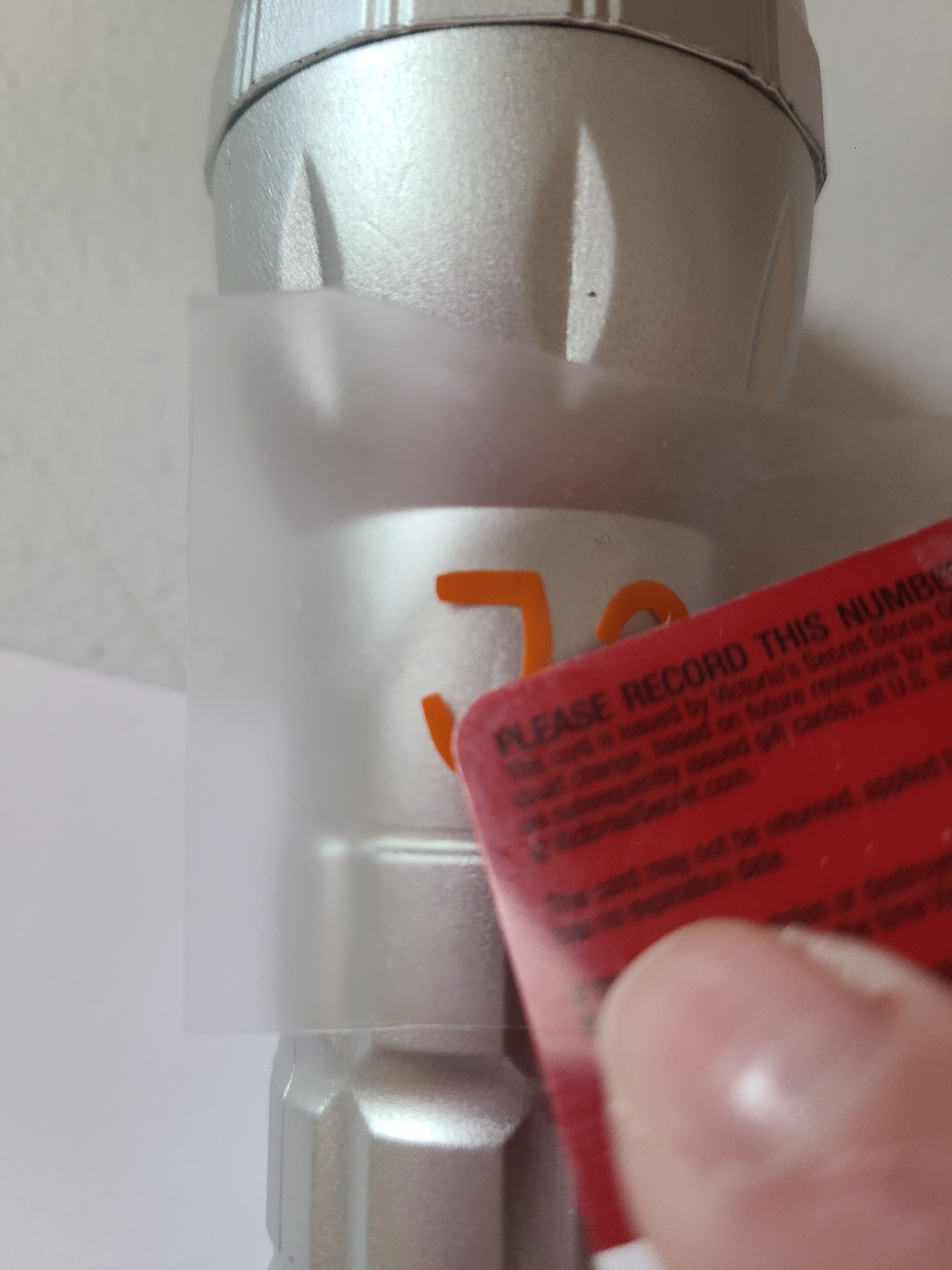 Going over vinyl letters with a credit card to apply them to a small flashlight with transfer tape to personalize it and send in a summer camp care package.