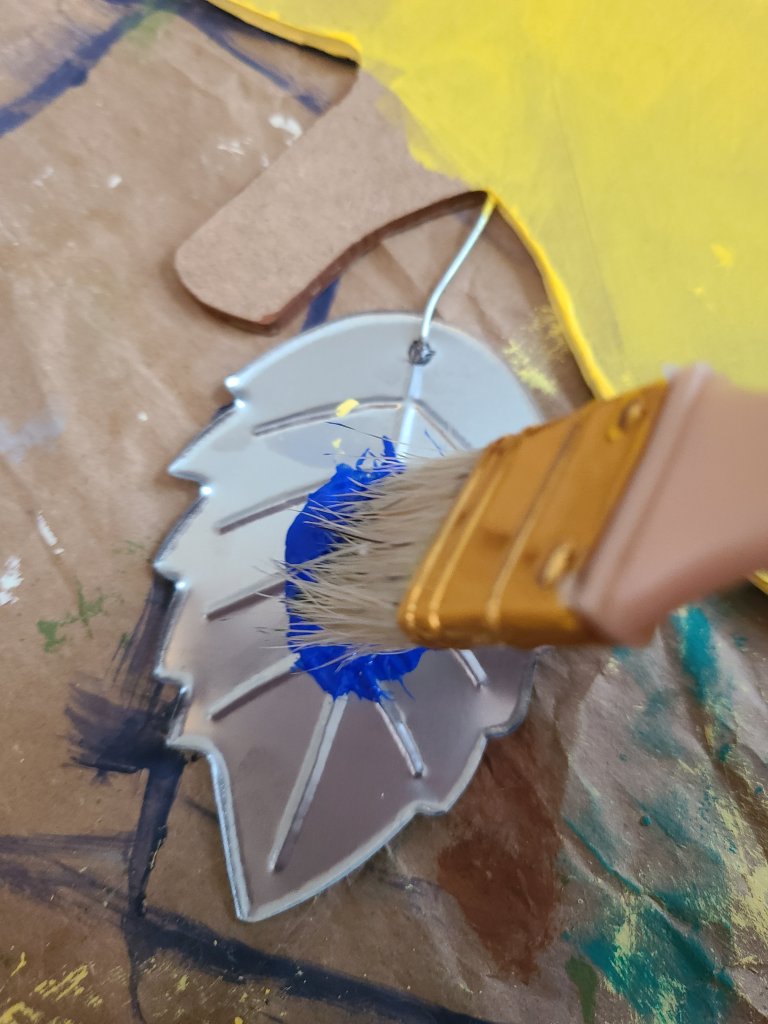 Leaf on the teacher door hanger being painted royal blue using a paint brush.