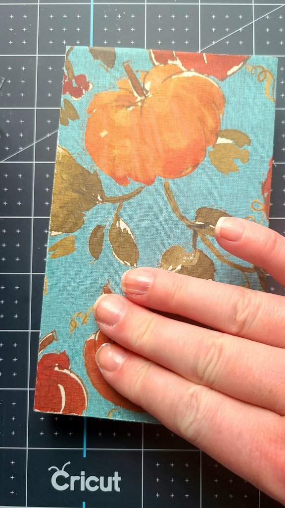 Using my fingers to place cardstock with pumpkins on it on to the piece of wood, and smoothing out any wrinkles and bubbles.
