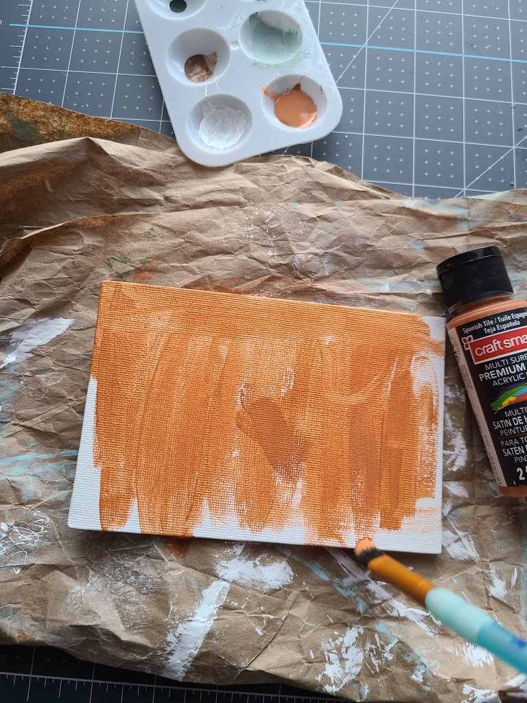 The canvas that will be the sign on the DIY fall centerpiece is being painted burnt sienna.
