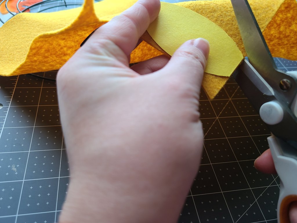 Paper leaf shape laid on top of mustard colored felt being cut out to go on the felt leaf wreath.