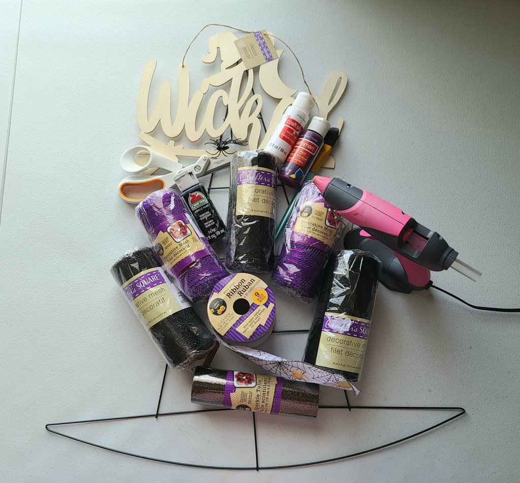 Supplies for Dollar Tree witch hat: wood "Wicked" sign, scissors, acrylic paint & paint brushes, hot glue gun, black and purple deco mesh, 2,5" ribbon, wire witch hat wreath form.