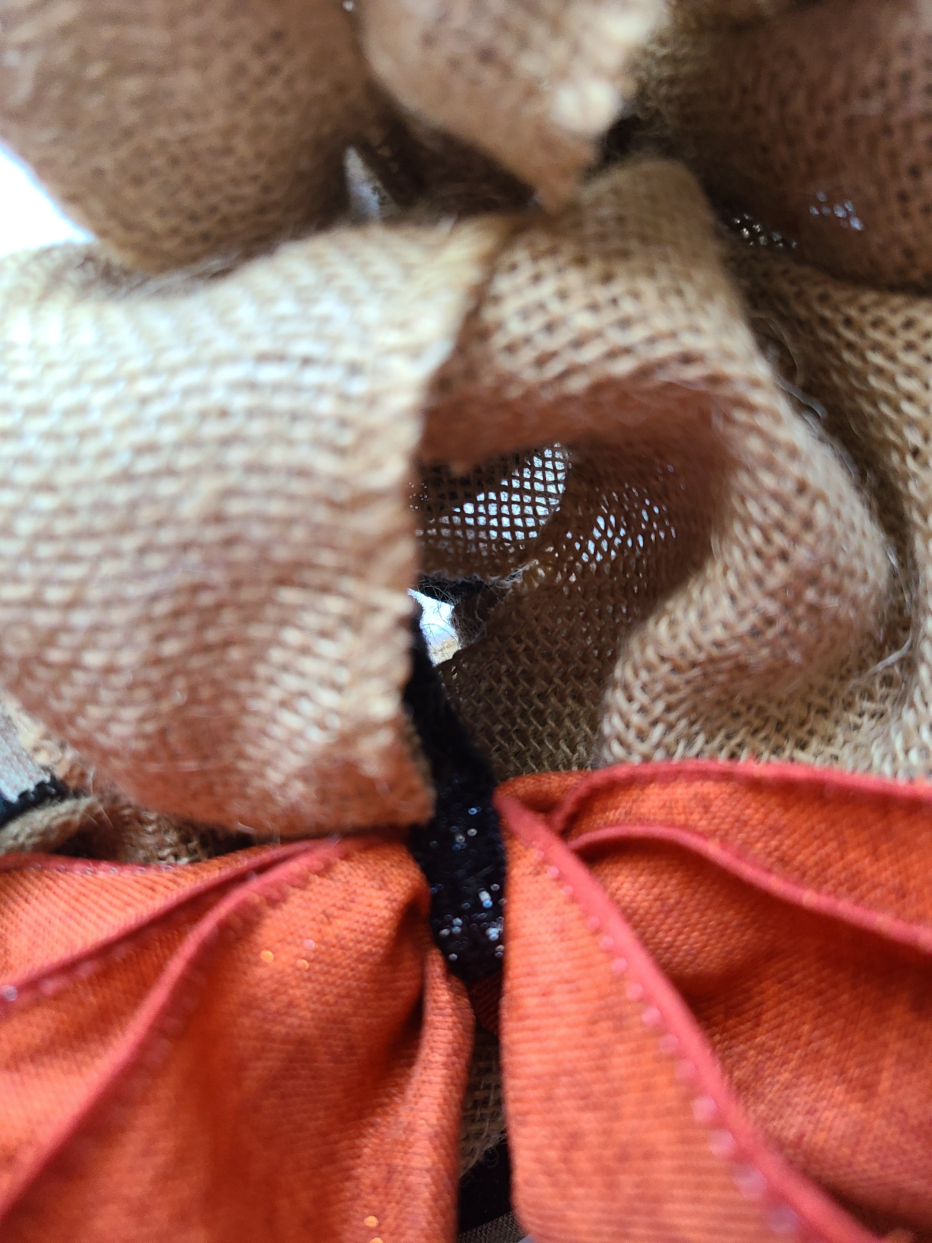 Attaching an orange bow to the burlap witch hat wreath with a black pipe cleaner.