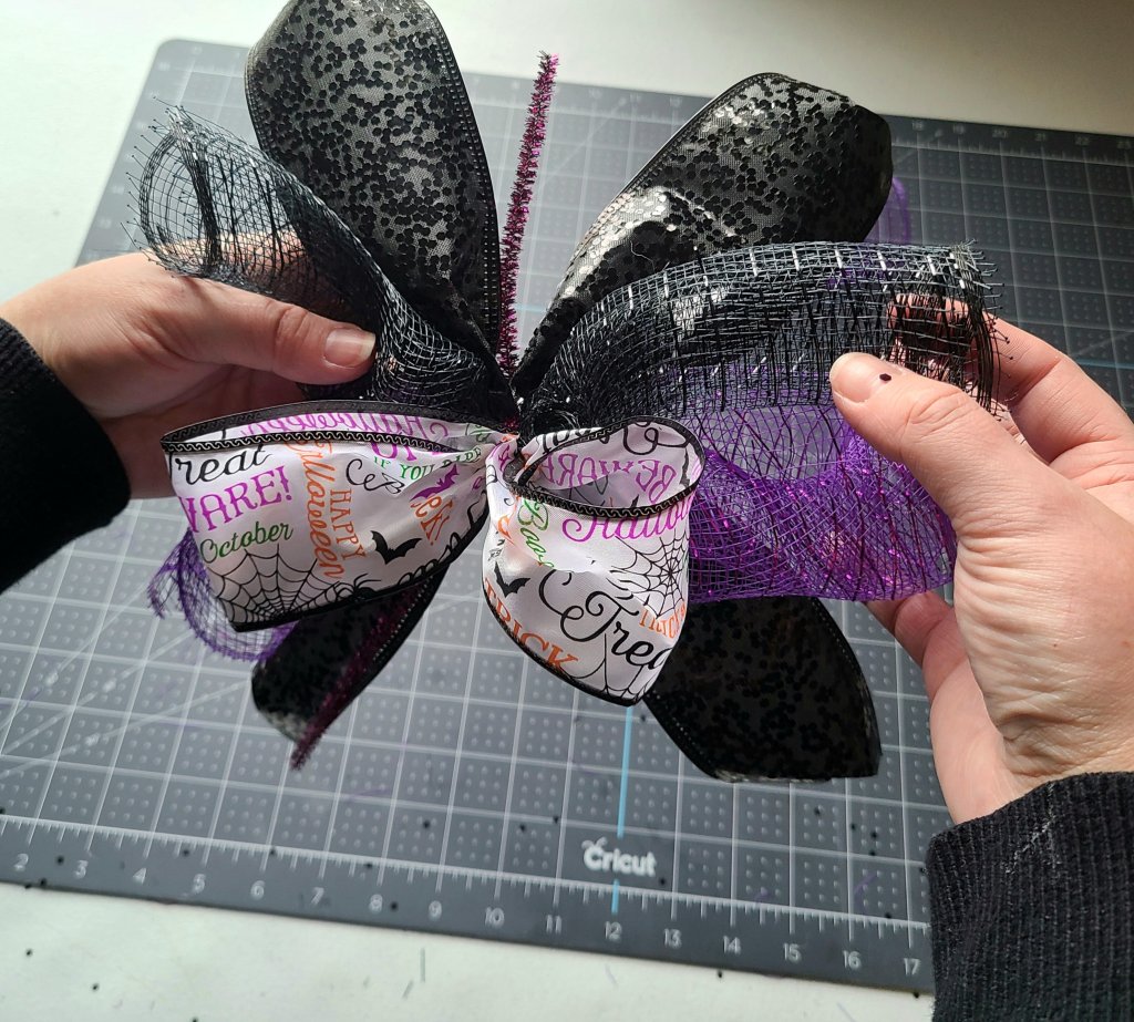 Bow for the Halloween pumpkin wreath with the bow, four deco mesh spirals, and black sequin ribbon attached to it.