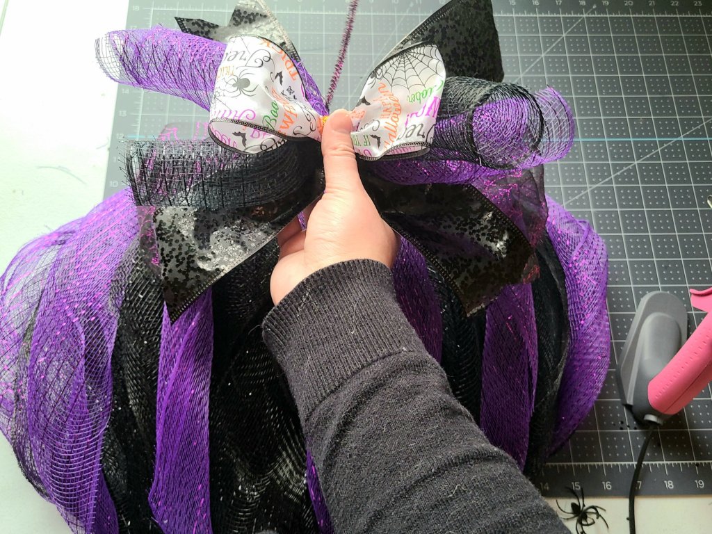 Adding the bow to the middle deco mesh piece on the Halloween pumpkin wreath.