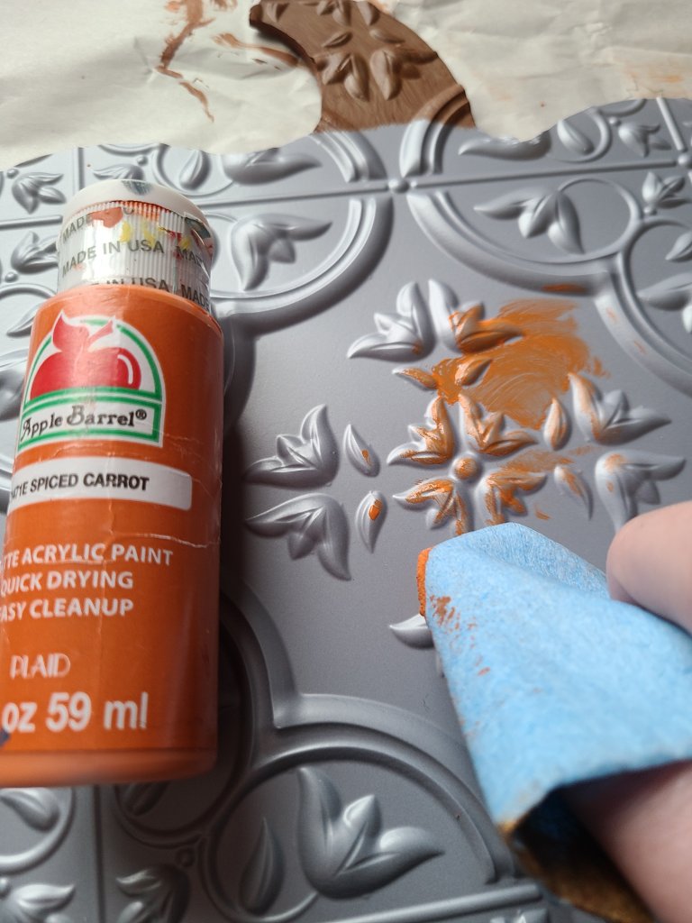 Thick blue paper towels made for automotive being used to apply orange acrylic paint to the tile on the fall pumpkin sign in circular patterns.