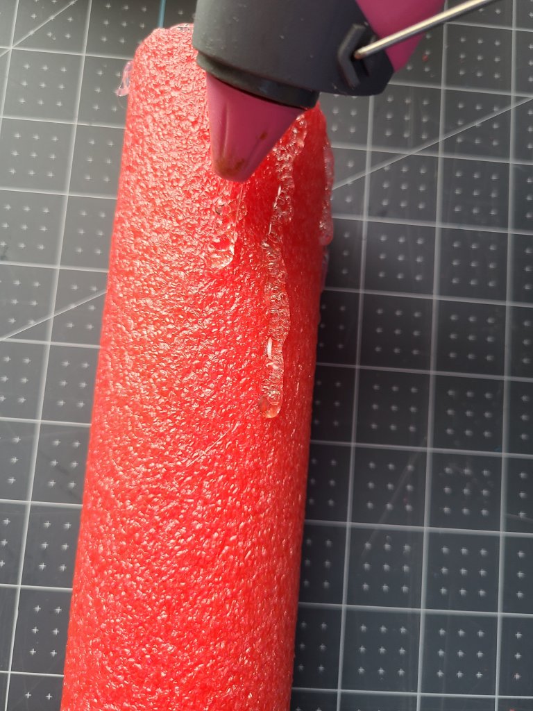 Using the hot glue gun to squeeze a line of glue down the front of the cut pool noodle. This will look like wax running down in the Halloween candle centerpiece.