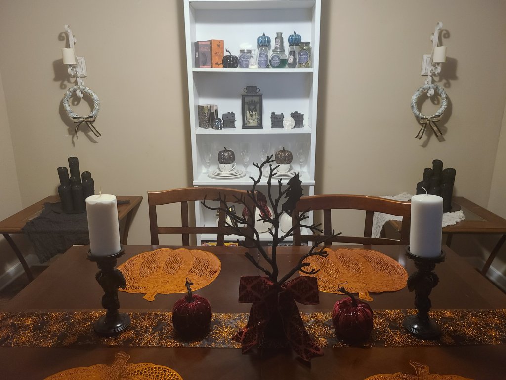 My dining room decorated for Halloween with one Halloween candle centerpiece on each of the two side tables next to the white bookcase.