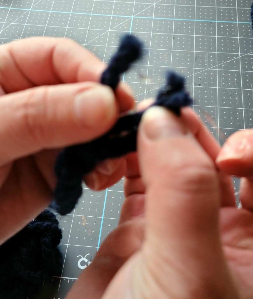 Pressing the right piece of yarn onto the glue on the middle one to seal the braid for the braided yarn pumpkin.