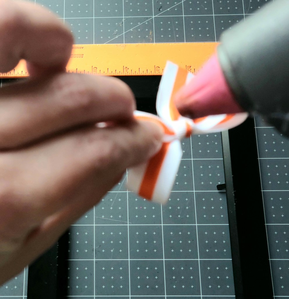 Adding hot glue to the back of a tiny bow to put on the frame which is part of the Halloween gift idea.