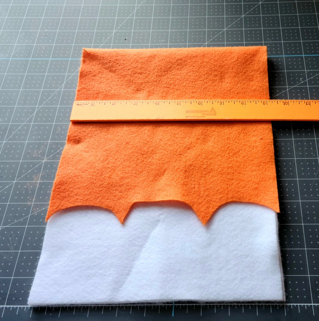 A ruler across the middle of the orange piece of felt that will be the flap on the no sew felt gift bag.