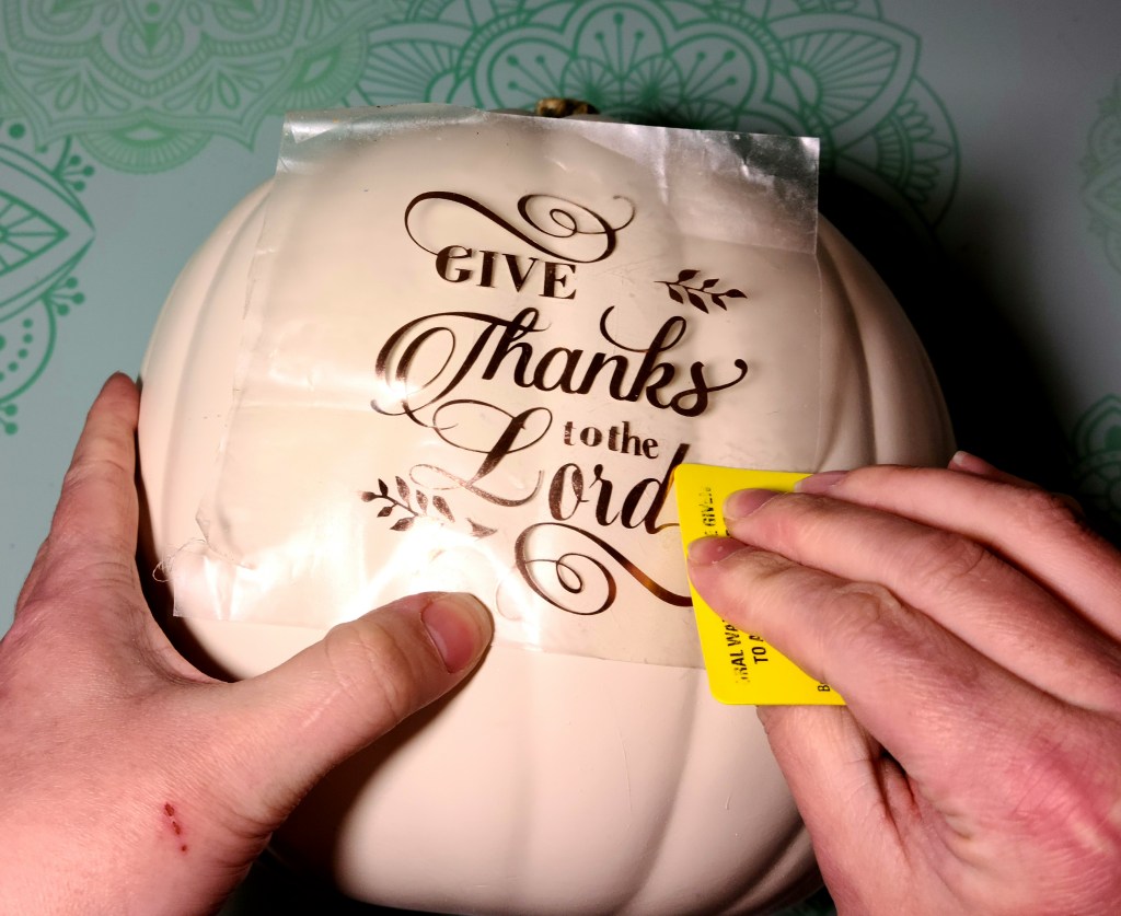 Using a credit card to go over the design to transfer it on to the gratitude pumpkin.