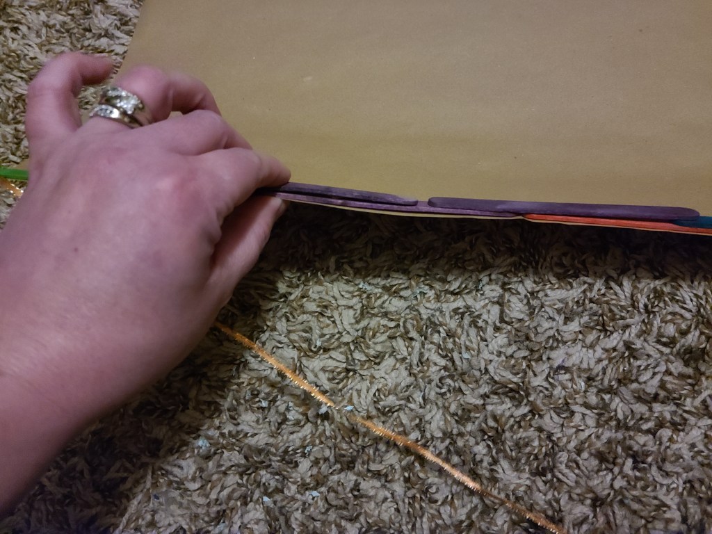 Gluing a second row of popsicle sticks across the top of the scroll wall hanging.
