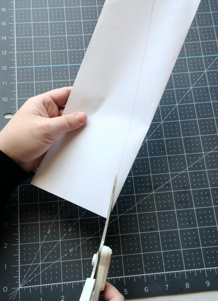 Cutting along a diagonal line a piece of white paper that's folded in half to form a triangle. It will become the pattern for your fabric Christmas tree.  
