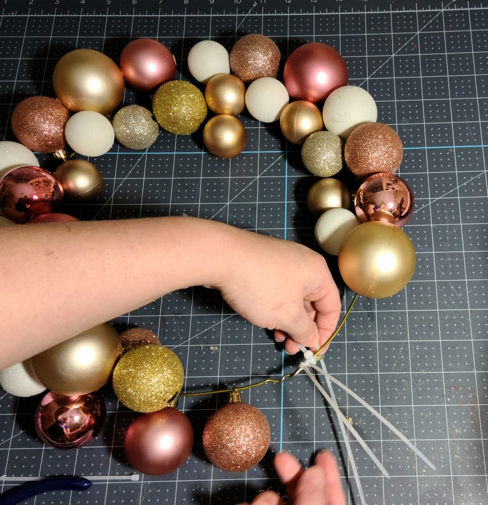 Adding a fourth zip tie to secure the Christmas ornament wreath.