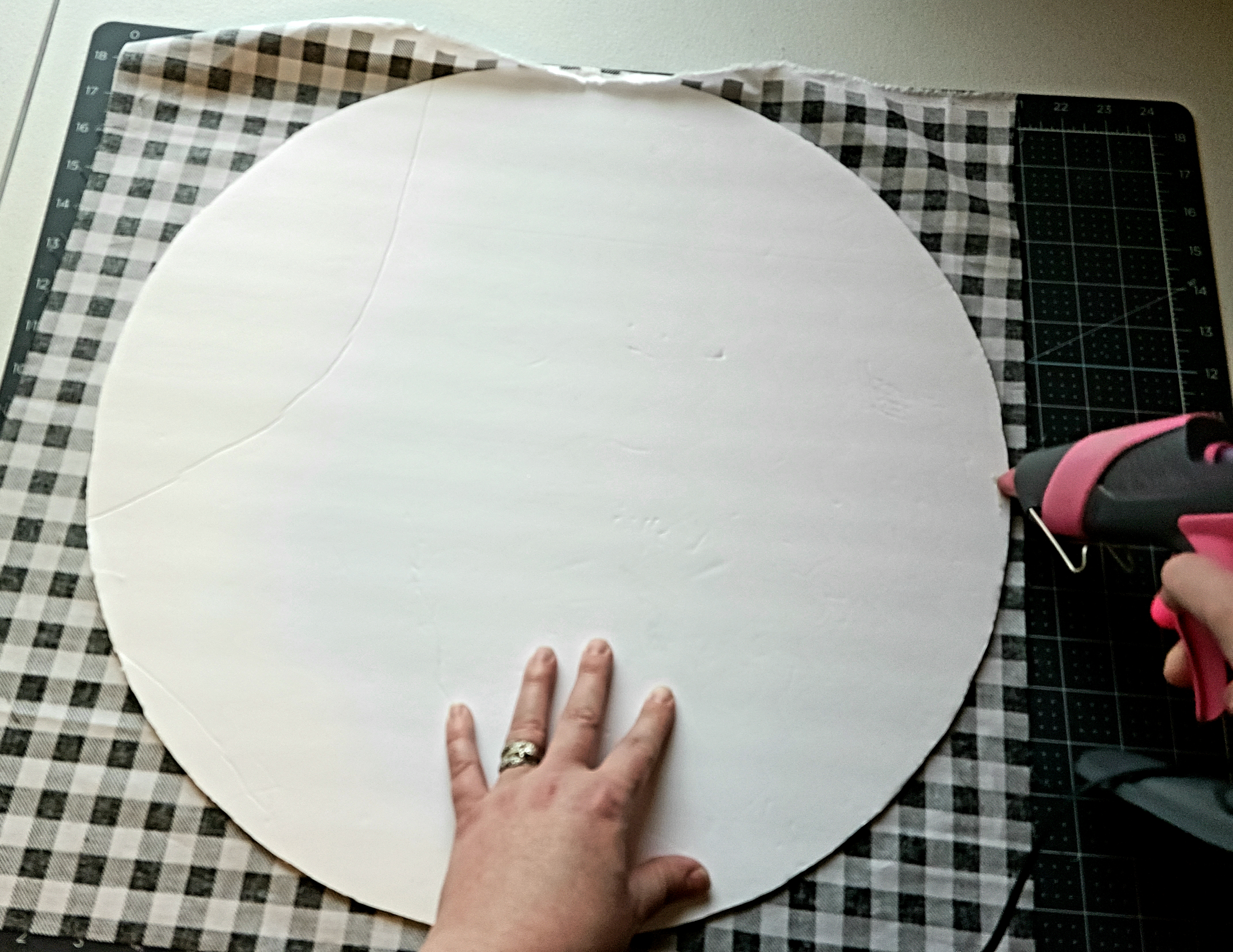 Putting hot glue on the back of the round Christmas sign to attach the fabric. 