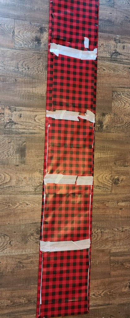 Five 11x14 Cardboard pieces wrapped with red and black buffalo check wrapping paper taped together to form a DIY Christmas tree collar.
