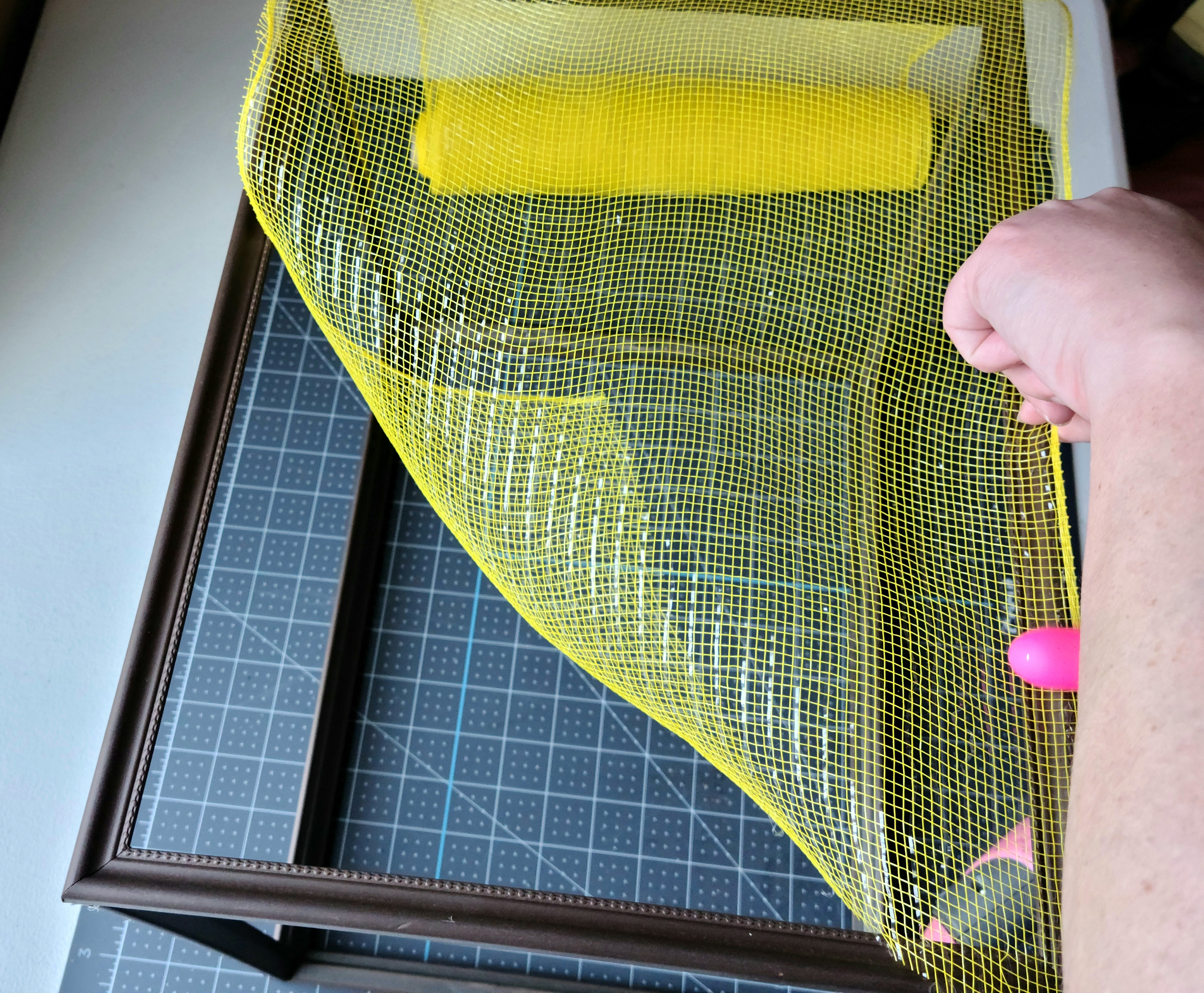 Pressing the deco mesh on the hot glue that was added on the frame of the DIY lighted gift box.