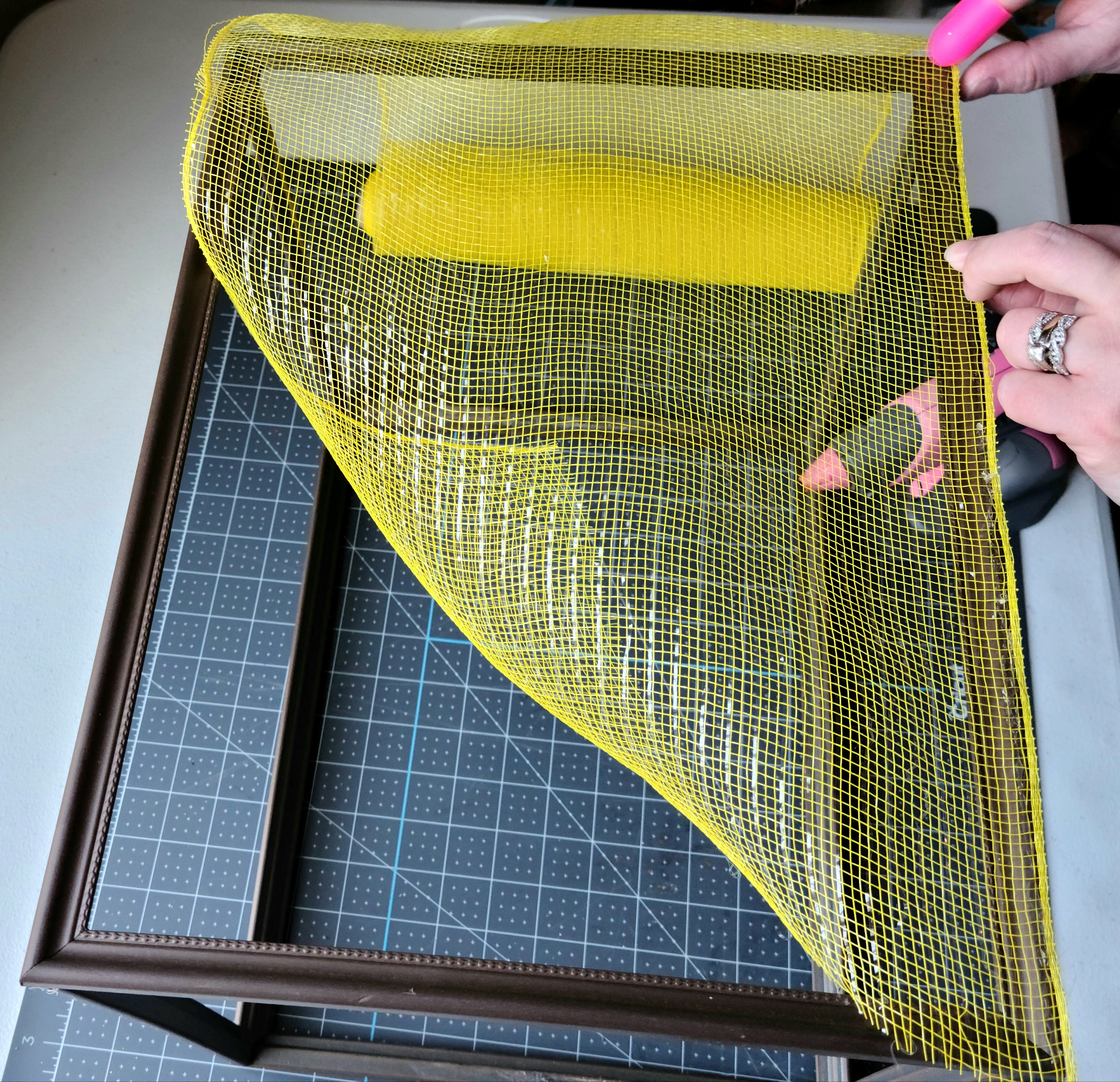 Pressing the deco mesh on the hot glue that was added on the frame of the DIY lighted gift box. The first side on the box is now glued down.