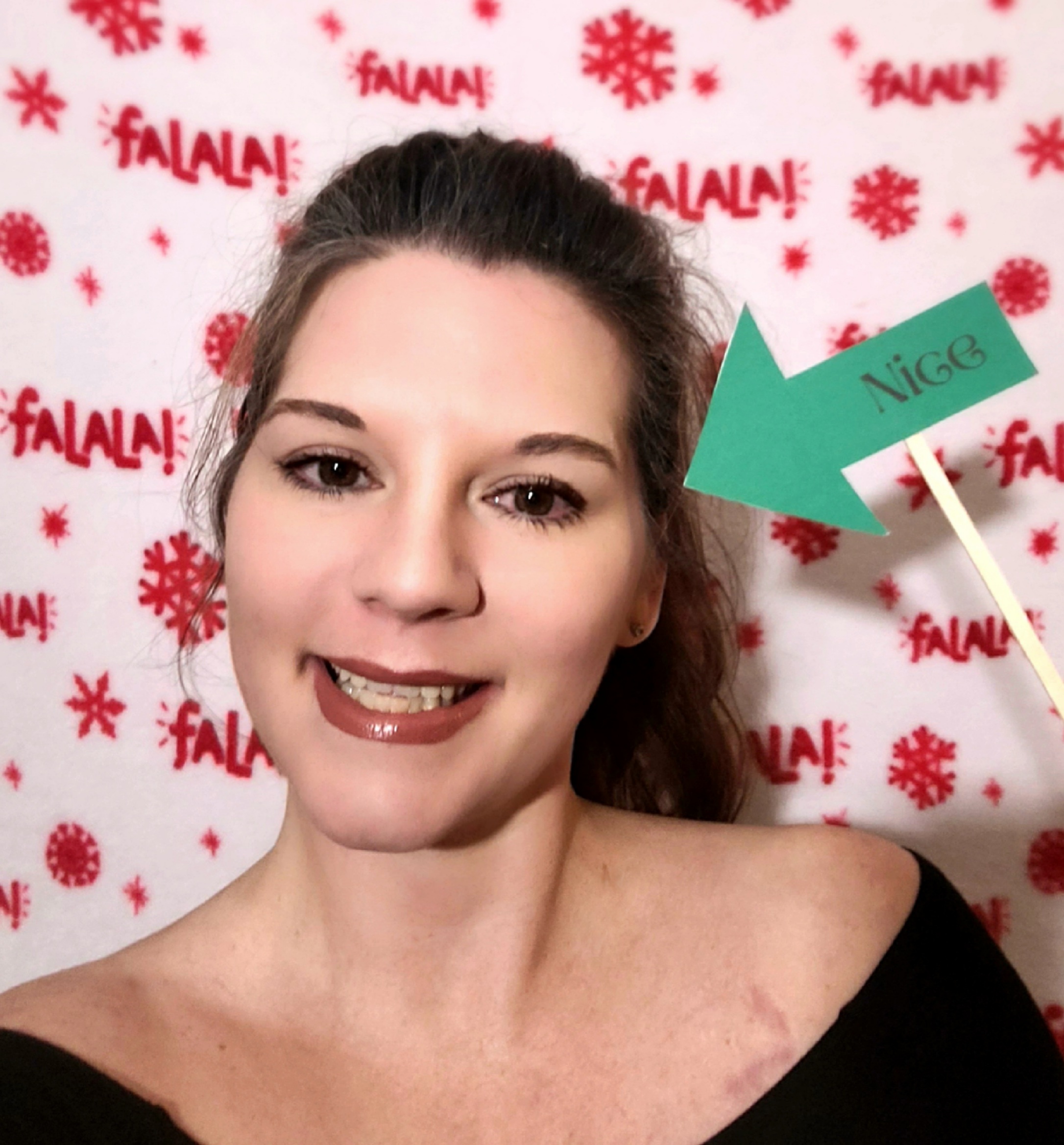 Me with a "Nice" arrow prop in the DIY Christmas photobooth set up with a Christmas blanket backdrop on Elf family movie night.