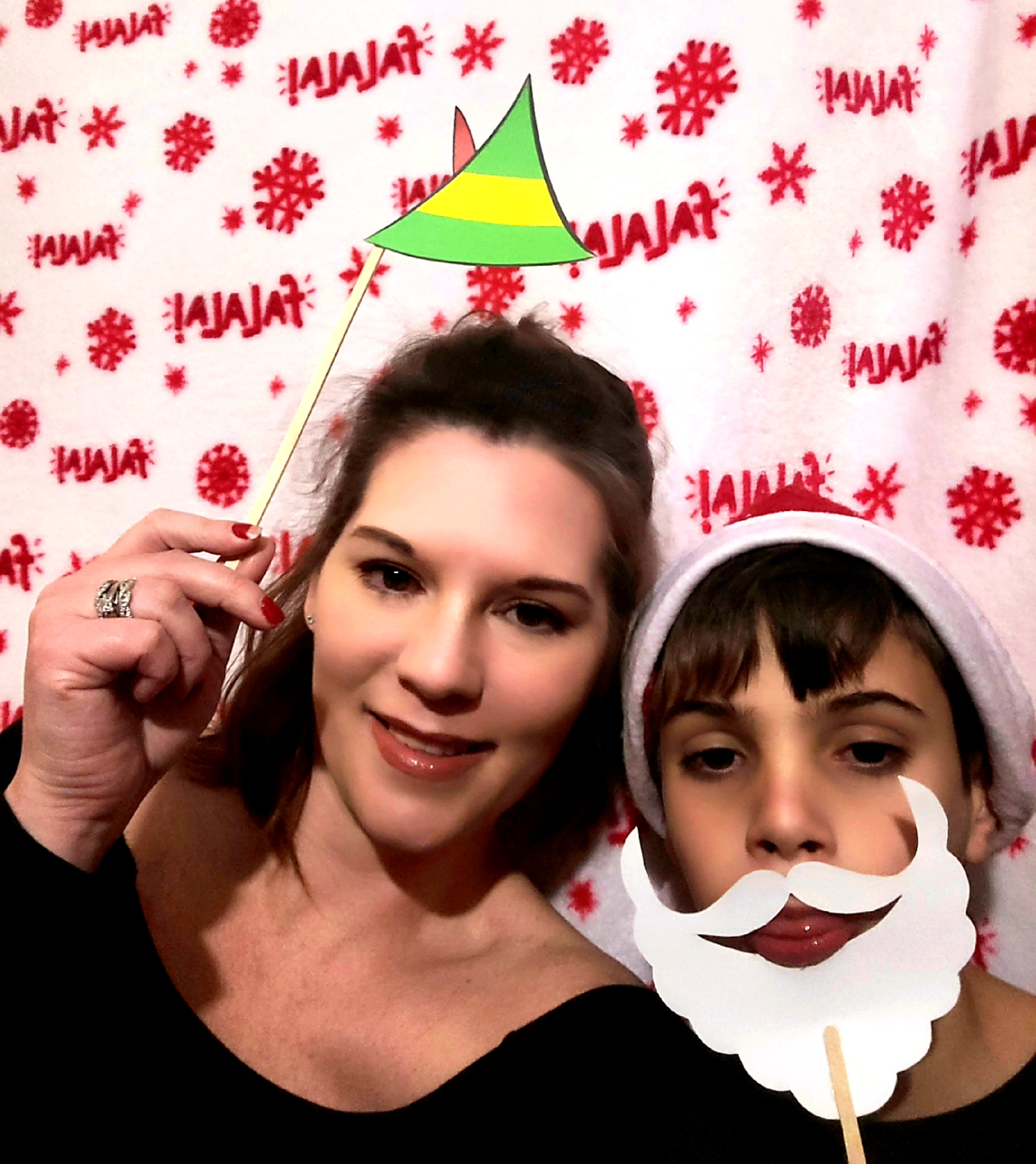 My son and I with a Buddy the Elf hat prop and a Santa beard and hat prop in the DIY Christmas photobooth set up with a Christmas blanket backdrop on Elf family movie night.