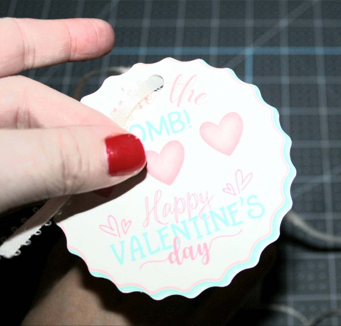 Feeding white ribbon through the Valentine's Day teacher's gift tag.