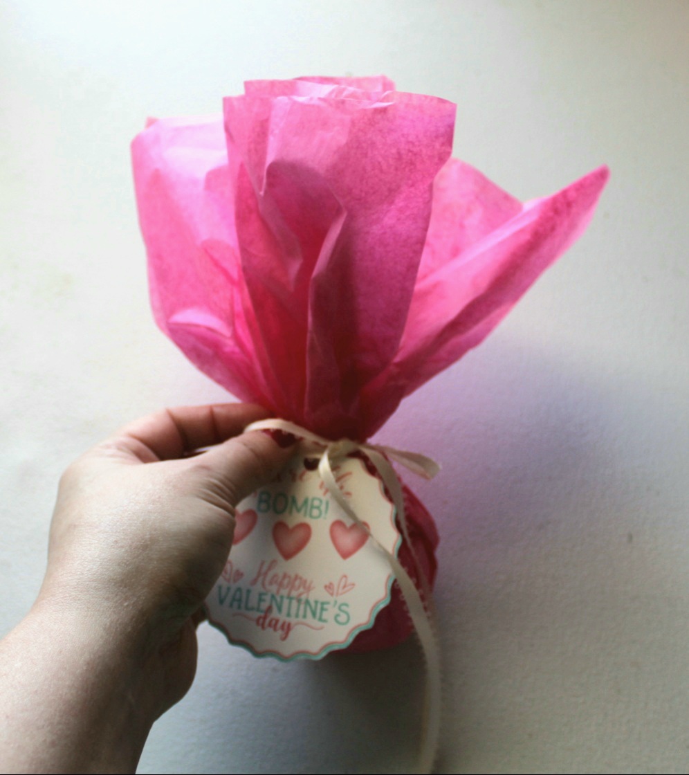 Tying a ribbon in a bow around the tissue paper gift wrap to close the Valentine's Day teacher gift.