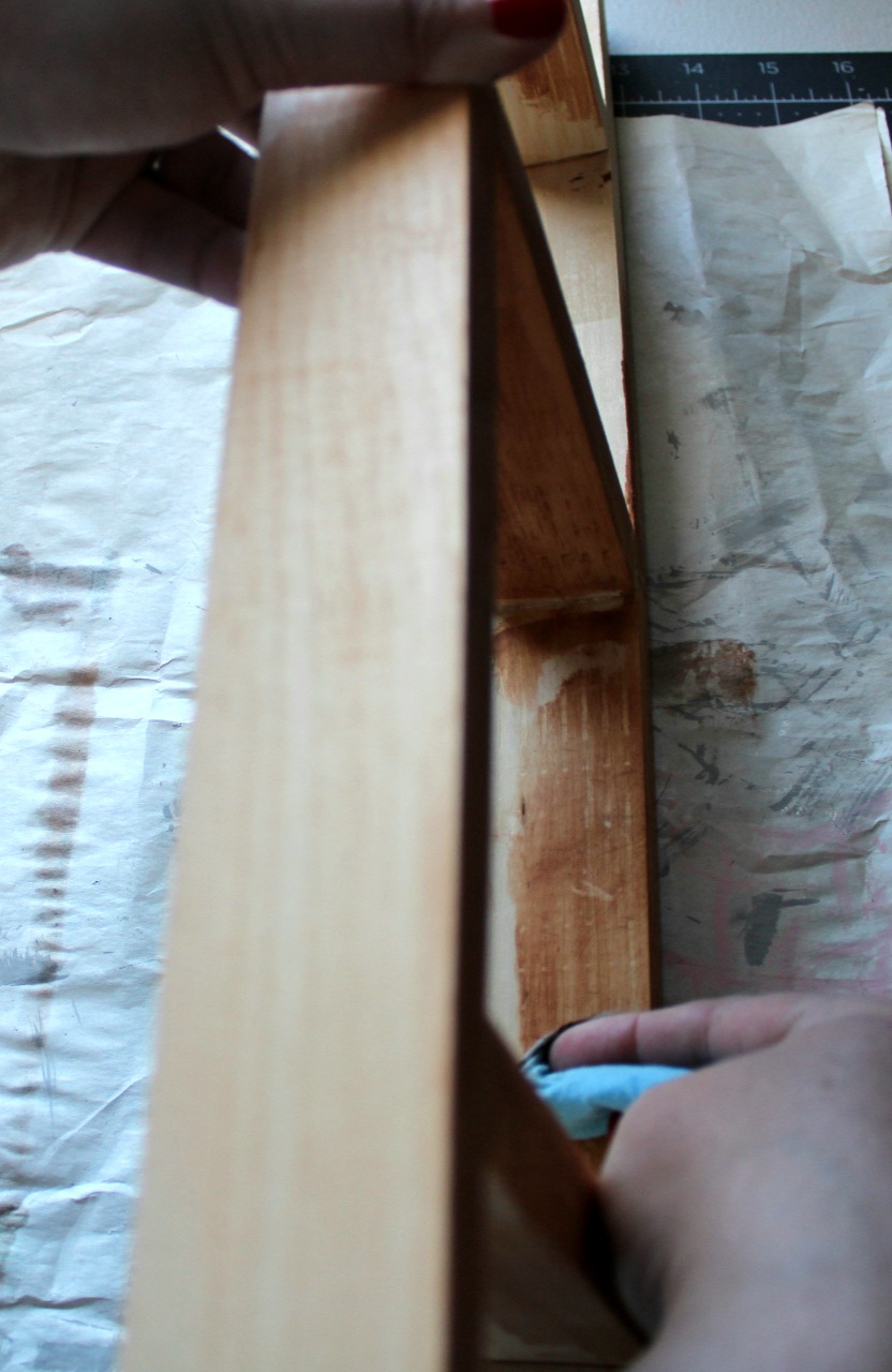 Wiping paint stain on the DIY tea towel ladder with a paper towel.
