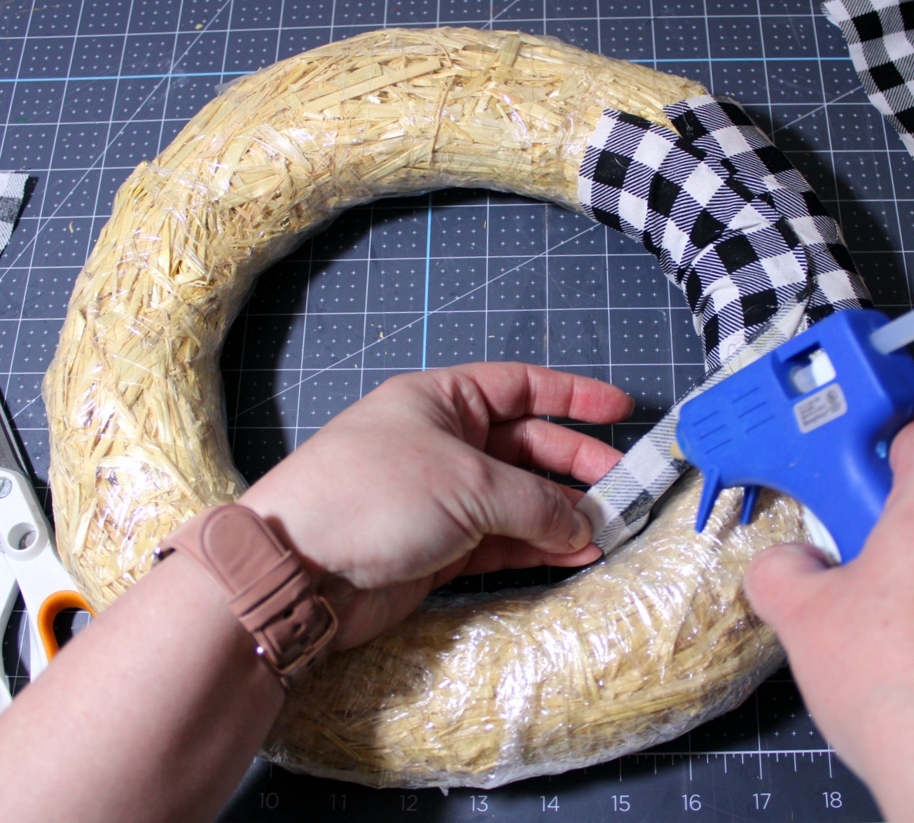 Attaching black and white buffalo check fabric to a straw wreath form with hot glue.