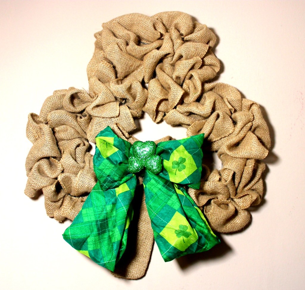 Burlap shamrock wreath with green scarf tied as a bow above the stem and a glitter shamrock embellishment in the bow.