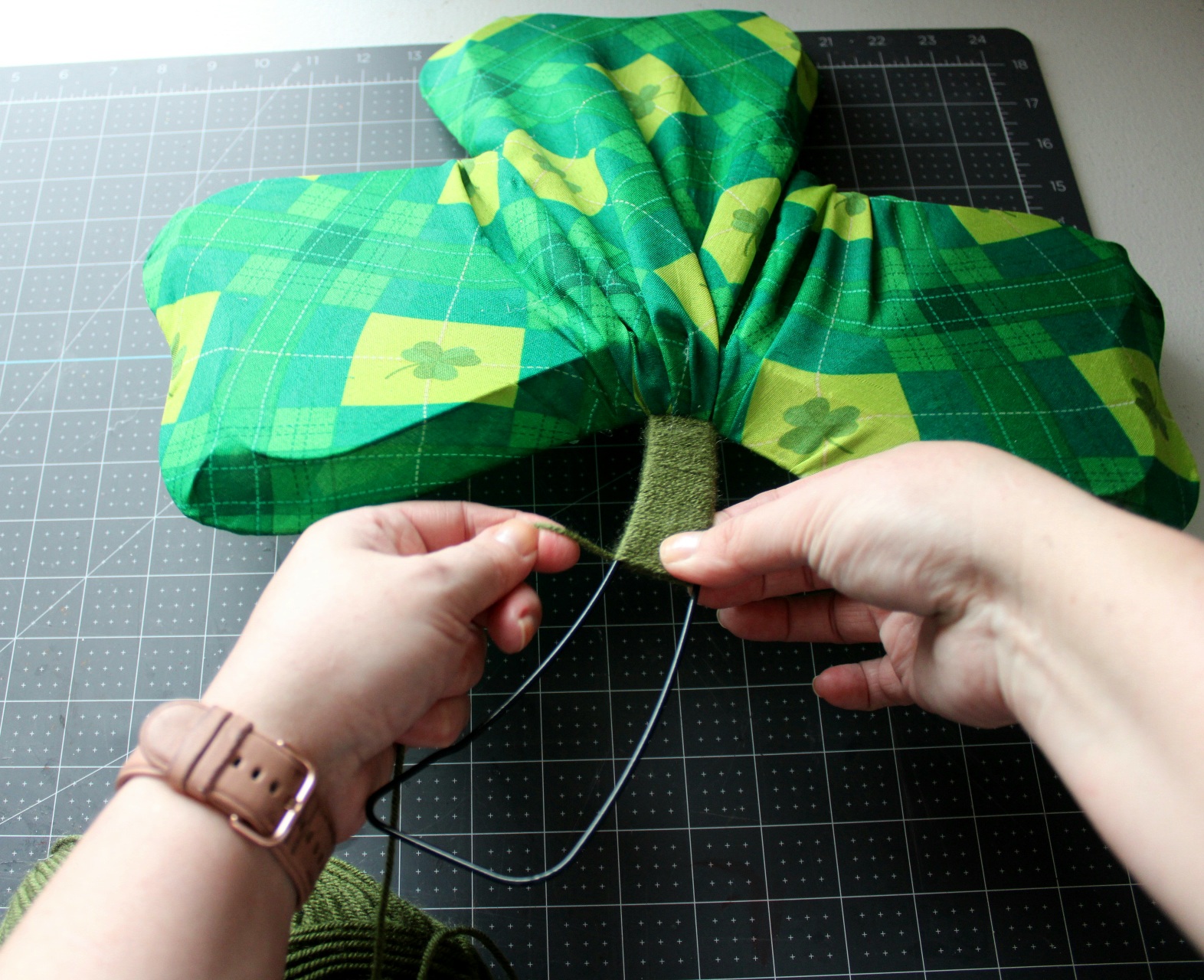 Wrapping moss green yarn around the stem of the DIY shamrock wreath form.