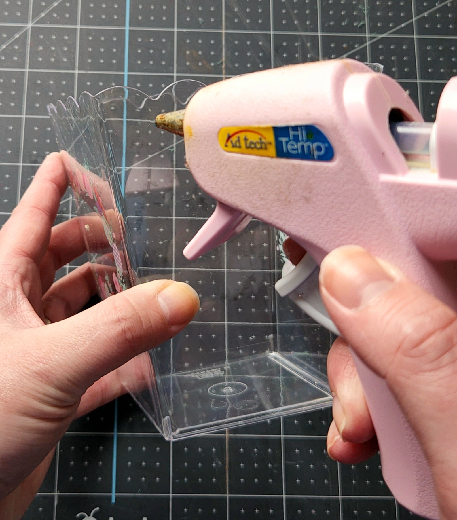 Pressing the hot glue gun through the clear vase to put a hole in it to hang on the door hanger.