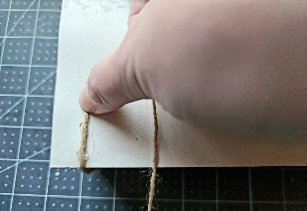 Placing twine on the dab of hot glue on the bottom of the stack of books.